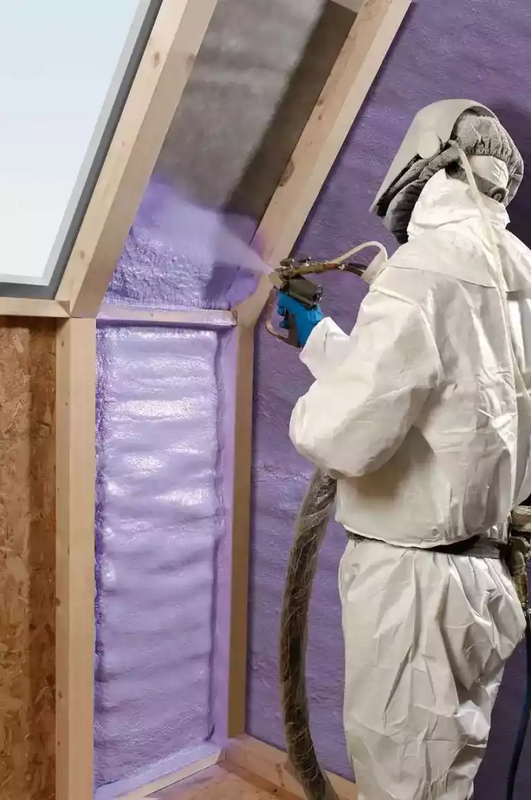 Un applicateur en combinaison projette une mousse isolante entre les montants d’une ossature bois.