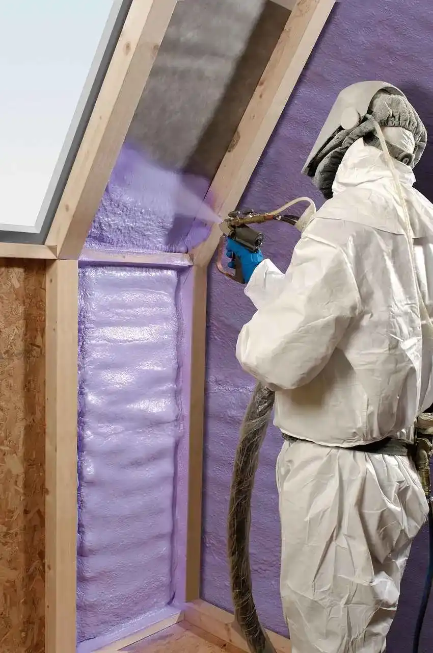 Un applicateur en combinaison projette une mousse isolante entre les montants d’une ossature bois.