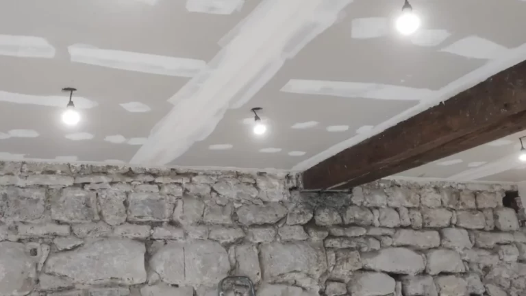 Mur de pierre mis à nu sur lequel repose une poutre en bois, sous un plafond fraîchement plâtré